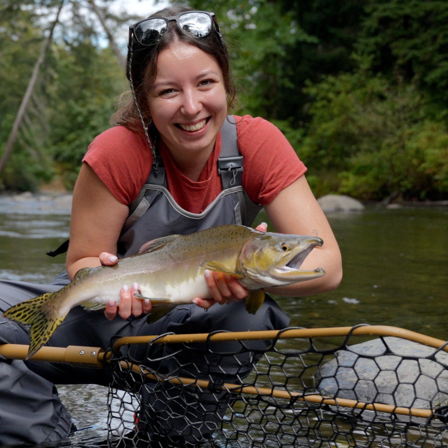 Woman holding a large fish by a river with a seam net