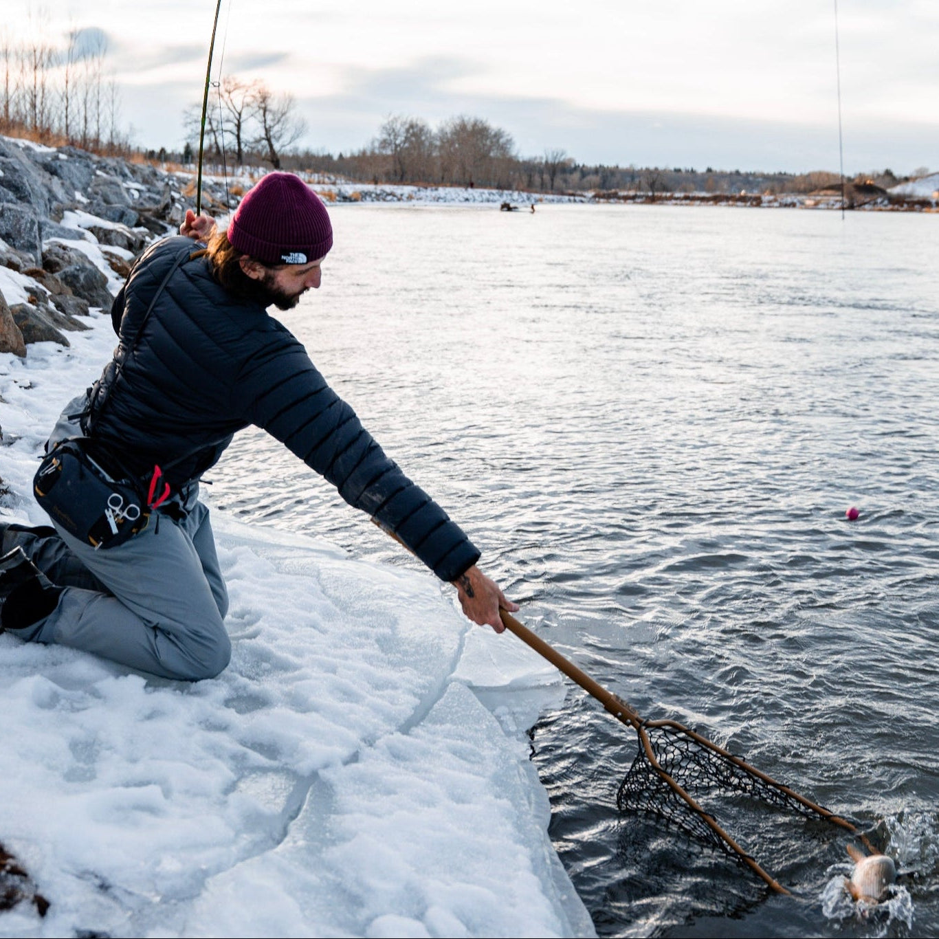 Person fly fishing on a frozen lake with a rod and net.