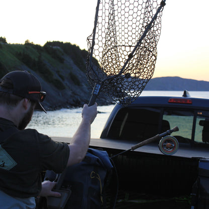 Person holding a seam fishing net over a car by a lake at sunset